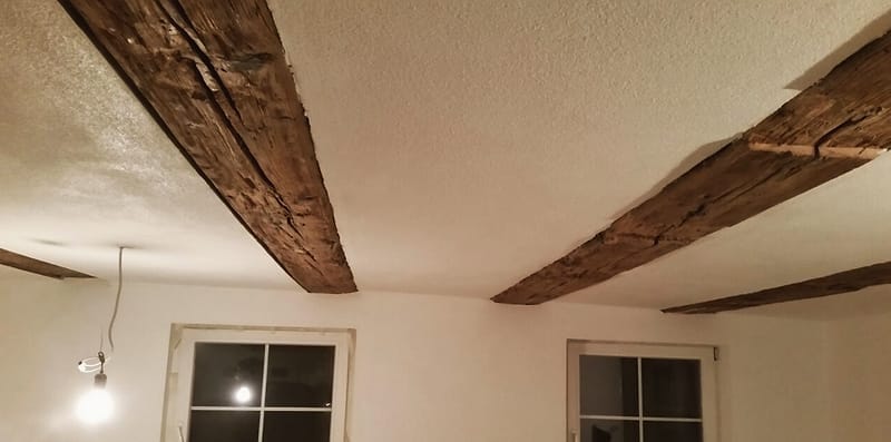 Sanierter Altbauraum: neu verputzte Wände und Decke, alte Holzbalken sichtbar erhalten
