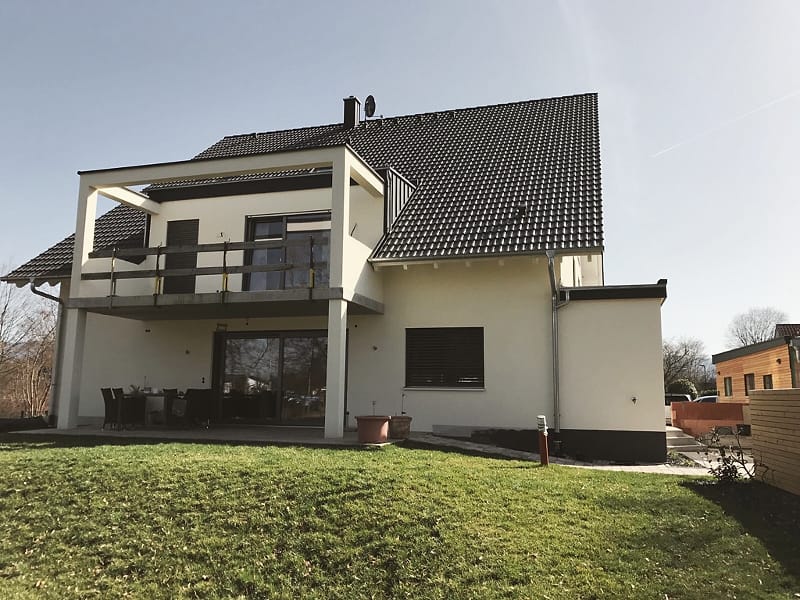 Wohnhaus mit hell verputzter Fassade, Balkon und Garten