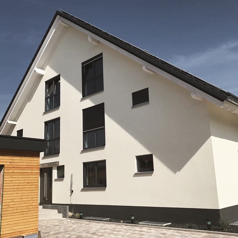 Wohnhaus mit hell verputzter Giebelfassade, dunklen Fenstern und Holzverkleidung